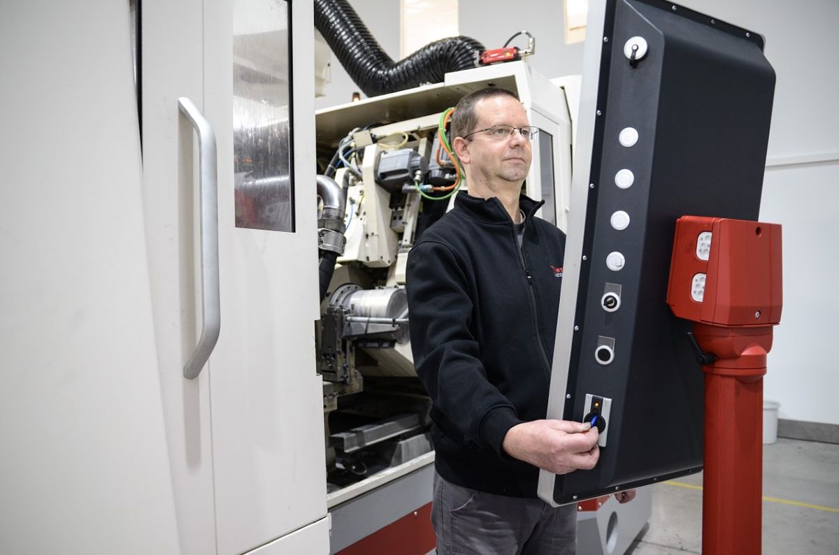 An operator stands in front of a large machine and uses a swivel-mounted HMI panel for control. The system is designed as an industrial machining center.