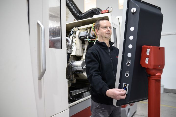 An operator stands in front of a large machine and uses a swivel-mounted HMI panel for control. The system is designed as an industrial machining center.