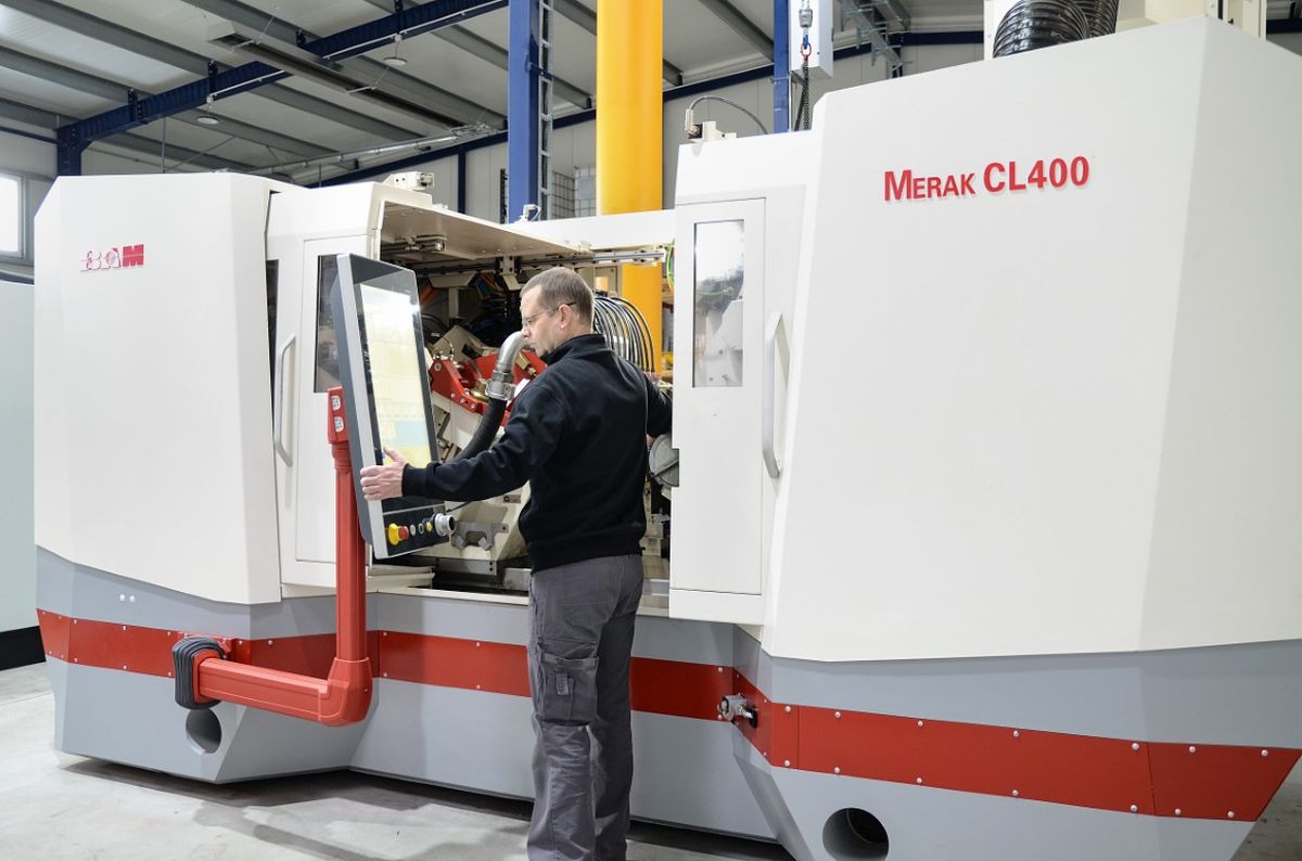 An operator stands in front of a large machine and uses a swivel-mounted HMI panel for control. The system is designed as an industrial machining center.