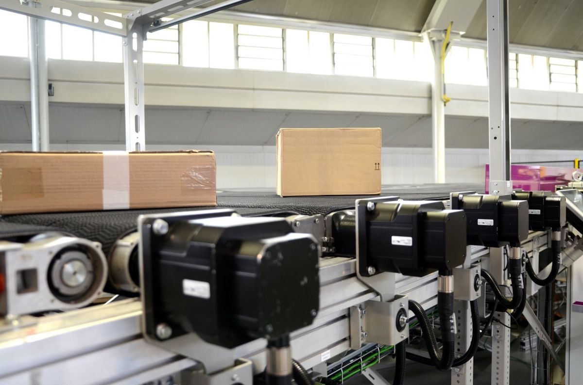 Nastro trasportatore con diversi pacchi e unità di azionamento elettriche in un moderno impianto industriale – simbolo di logistica automatizzata, flusso dei materiali preciso e tecnologia di controllo efficiente.