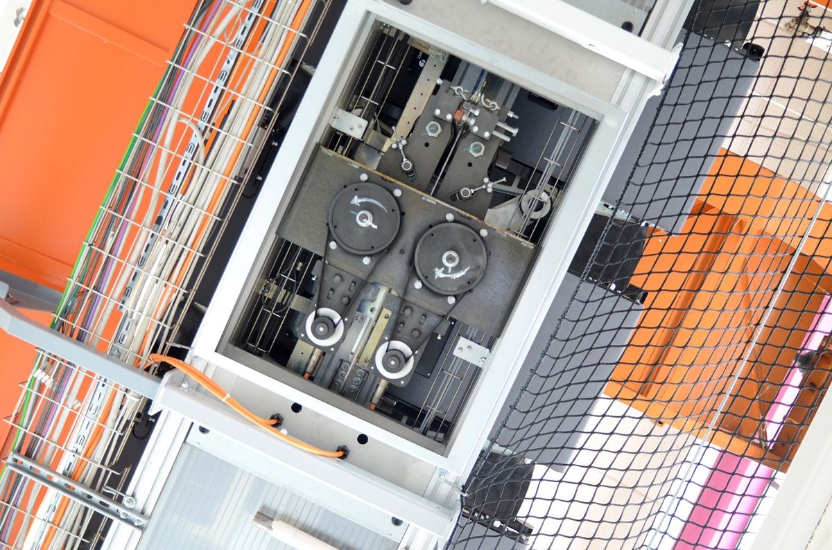 Vista di un sistema di azionamento meccanico con cinghie, pulegge e cablaggio dei sensori, protetto da una rete di sicurezza – simbolo di precisione, sicurezza e automazione industriale.