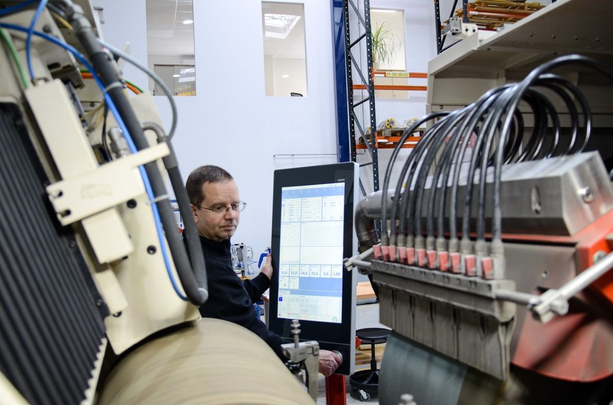 An operator stands between machines and interacts with a large touch HMI in a production environment. The setup includes complex wiring and industrial components.
