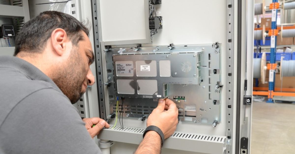 Qualitätskontrolle: Zwei Mitarbeitende in einer Fabrik inspizieren ein transparentes Kunststoffteil unter hellem Licht, mit Werkzeugen an einer Lochwand im Hintergrund.