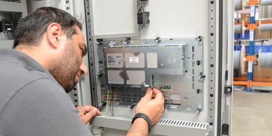 Qualitätskontrolle: Zwei Mitarbeitende in einer Fabrik inspizieren ein transparentes Kunststoffteil unter hellem Licht, mit Werkzeugen an einer Lochwand im Hintergrund.