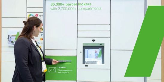 Eine Frau wirft einen Brief in den integrierten Briefschlitz der Paketstation ein.