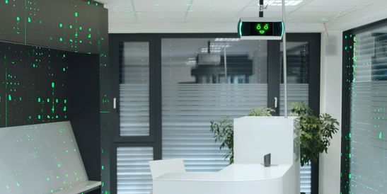 Moderne Bankfiliale mit Personen an Geldautomaten, KI-Assistent KeBob im Einsatz und Kunden beim Betreten durch Glastüren.