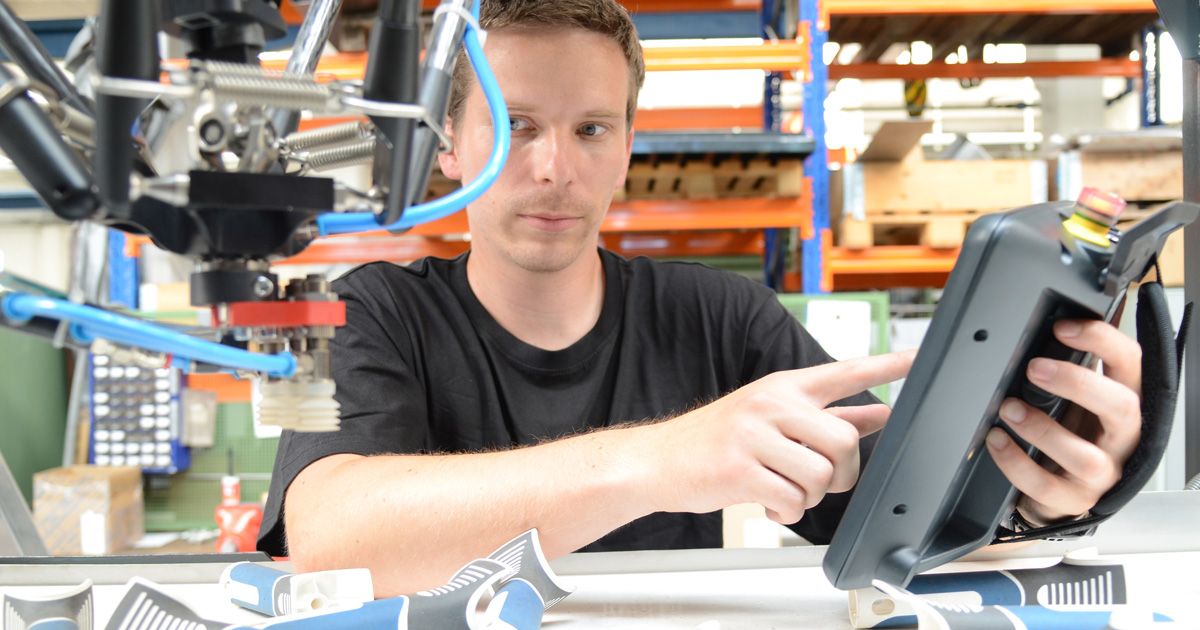 Jan Merkvart utilizza un HMI KEBA mobile all'interno di una cella robotizzata con un robot delta. I componenti in plastica vengono posizionati intorno a lui mentre controlla in modo sicuro le funzioni della macchina.