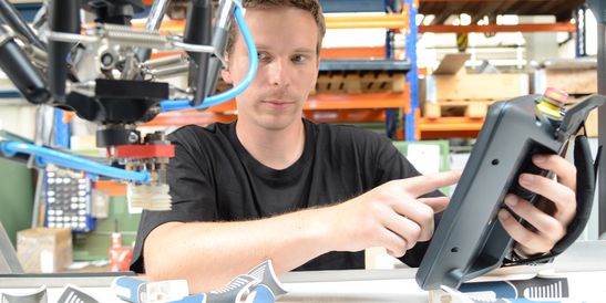 Jan Merkvart utilizza un HMI KEBA mobile all'interno di una cella robotizzata con un robot delta. I componenti in plastica vengono posizionati intorno a lui mentre controlla in modo sicuro le funzioni della macchina.