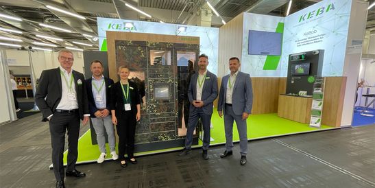 Fünf Personen stehen vor einem Messestand mit KEBA-Display und blicken lächelnd in die Kamera.