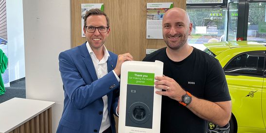 Christopher Karatsonyi (Carmaniac) und ein Vertreter von KEBA präsentieren gemeinsam eine KEBA-Wallbox mit grüner Dankesbotschaft im Rahmen der #GREENthankyou-Aktion.
