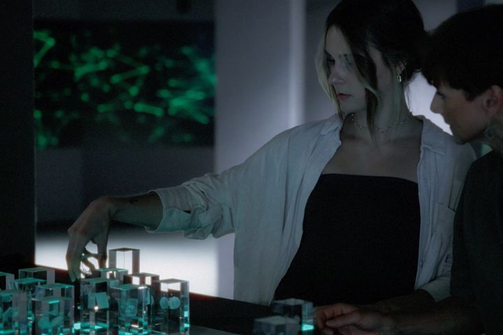 Zwei Frauen betrachten leuchtende Glaselemente in einer modernen, technologieorientierten Umgebung.