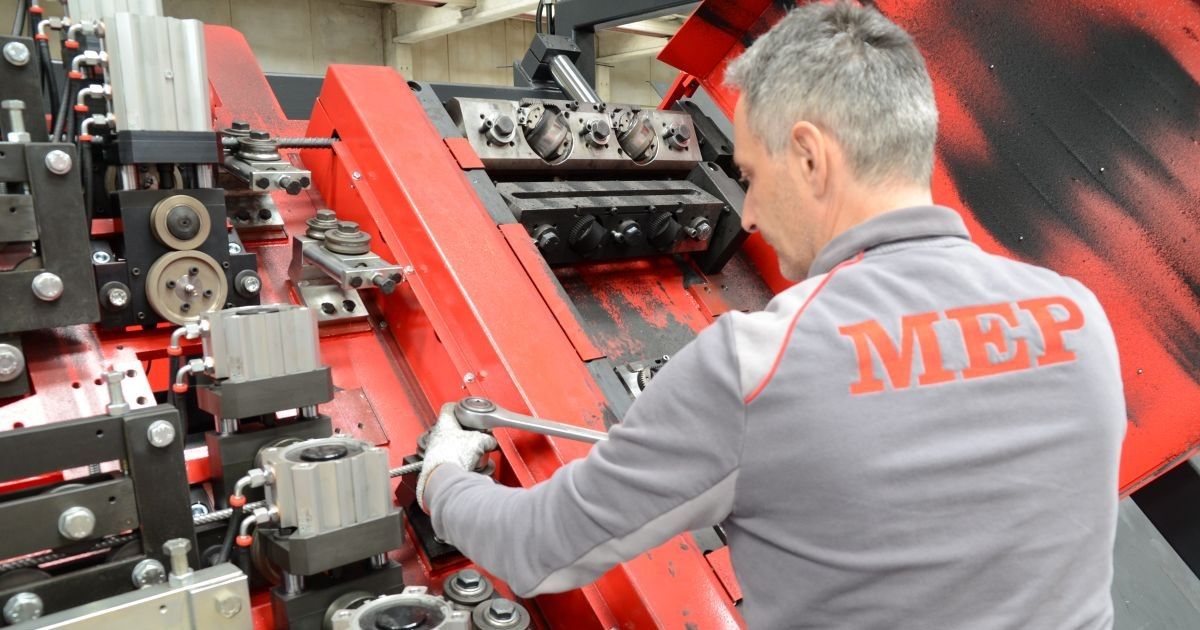 Ein Servicemitarbeiter führt Wartungsarbeiten an der Mechanik einer Maschine durch. Er justiert Komponenten mit einem Werkzeug.