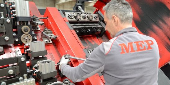 Ein Servicemitarbeiter führt Wartungsarbeiten an der Mechanik einer Maschine durch. Er justiert Komponenten mit einem Werkzeug.