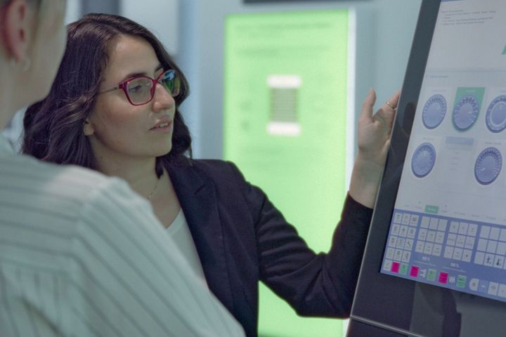 Eine Mitarbeiterin erklärt einer Kollegin eine industrielle Steuerung über ein modernes Touchpanel mit der Benutzeroberfläche von KEBA.