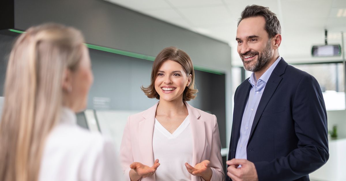 A man and a woman are speaking with a customer in the bank foyer