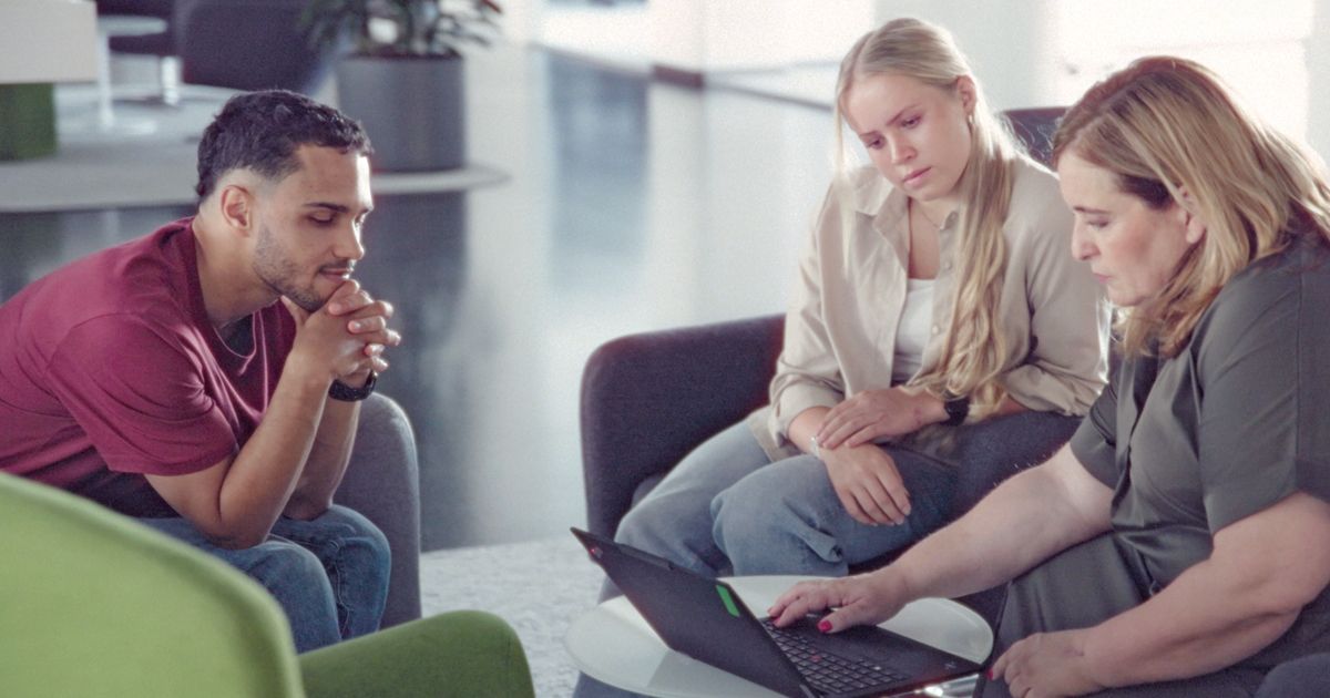 Drei Personen besprechen gemeinsam Inhalte auf einem Laptop in einer modernen Büroumgebung.