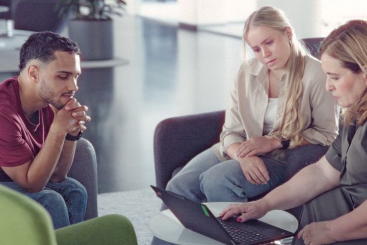 Drei Personen besprechen gemeinsam Inhalte auf einem Laptop in einer modernen Büroumgebung.