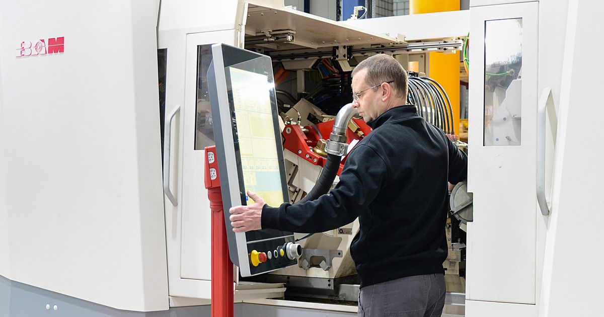 An operator stands in front of a large machine and uses a swivel-mounted HMI panel for control. The system is designed as an industrial machining center.