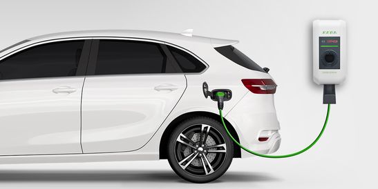 A white electric vehicle is being charged by a wall-mounted KEBA charging station. The green charging cable is connected to the car.
