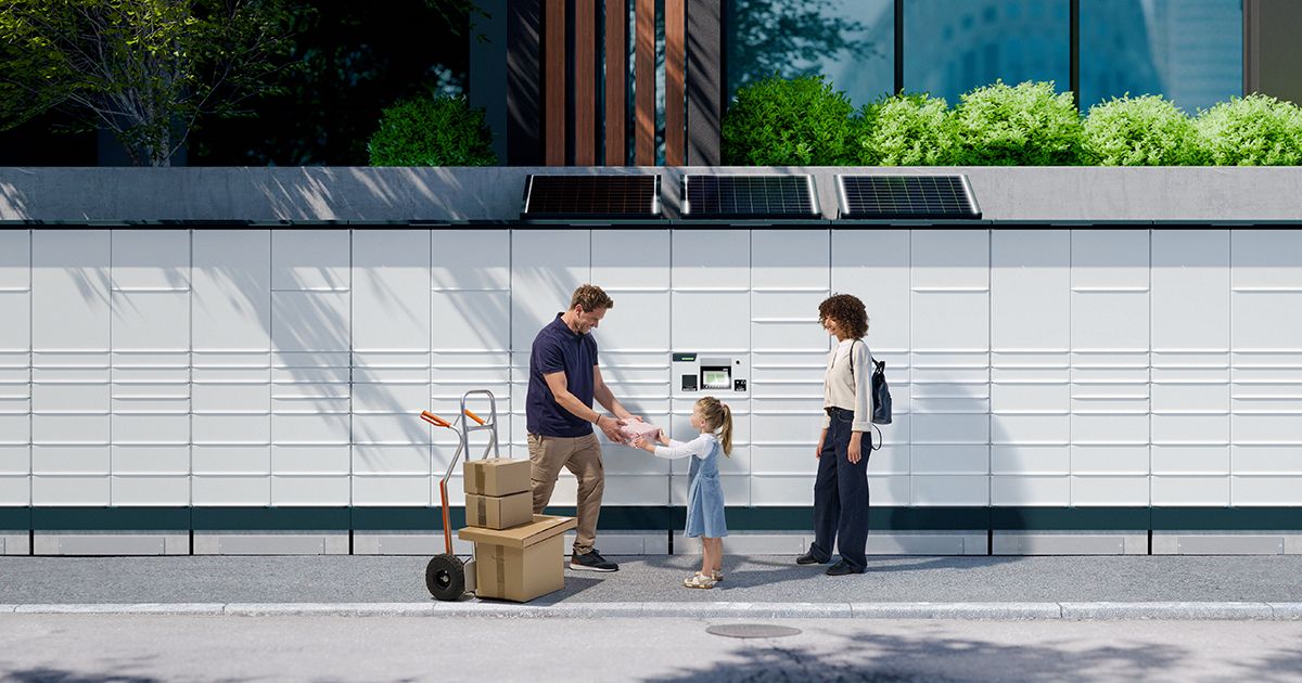 A family receives a package from a delivery person in front of a modern building with lockers and greenery.