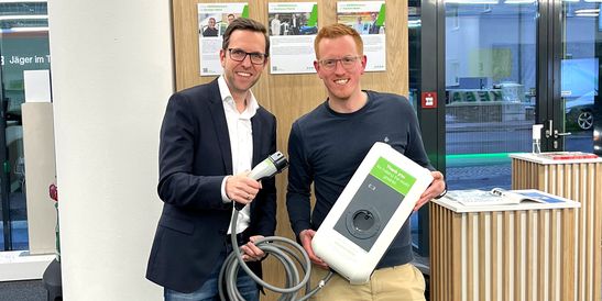 Two men present a KEBA wallbox and a charging cable as part of the #GREENthankyou campaign.