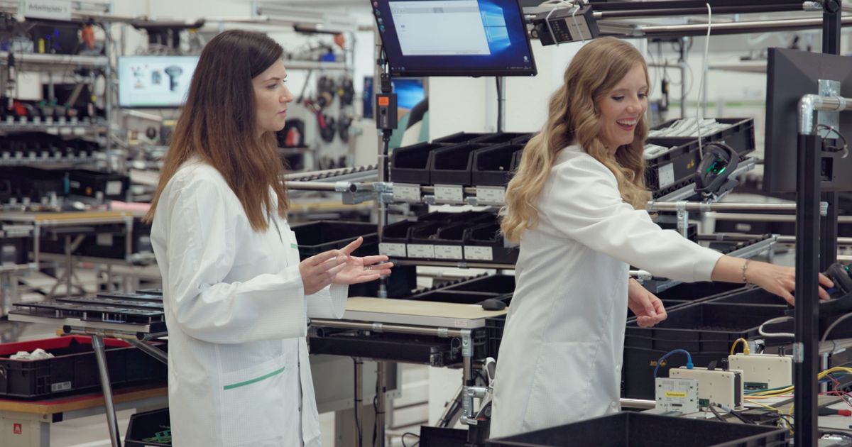 Zwei Mitarbeiterinnen in weißen Laborkitteln arbeiten gemeinsam in einer Elektronikfertigung.