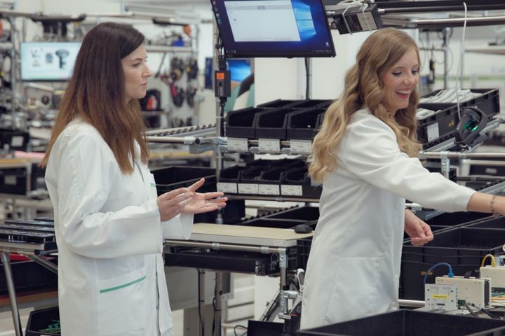 Zwei Mitarbeiterinnen in weißen Laborkitteln arbeiten gemeinsam in einer Elektronikfertigung.