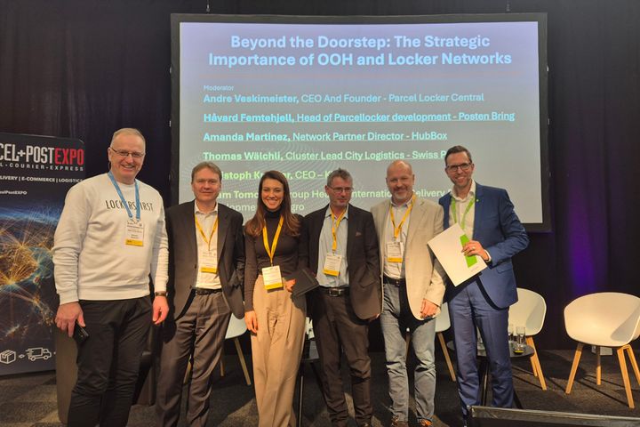 A group of six people standing on a stage at Parcel+Post Expo, with a presentation screen in the background.