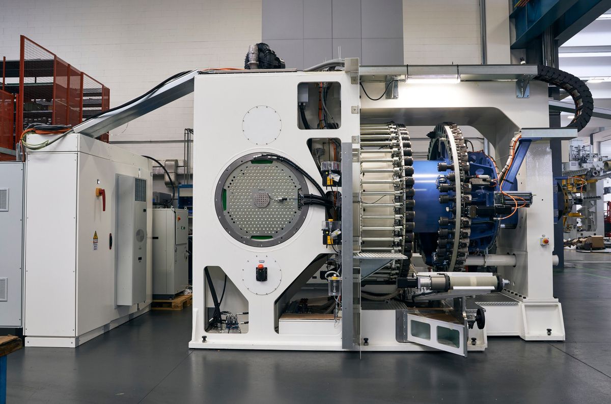 Large industrial production machine in a SPL manufacturing hall with a central drive and rotary system. The equipment is designed for industrial automation and precision control applications and is surrounded by several control cabinet and supply units. 