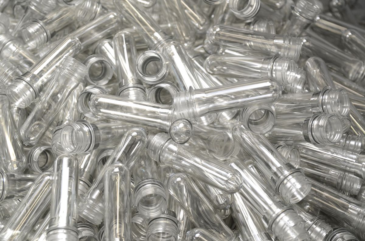Primo piano di numerosi preforme PET trasparenti per la produzione di bottiglie. L’immagine rappresenta la lavorazione precisa della plastica, la produzione efficiente e i processi produttivi automatizzati.