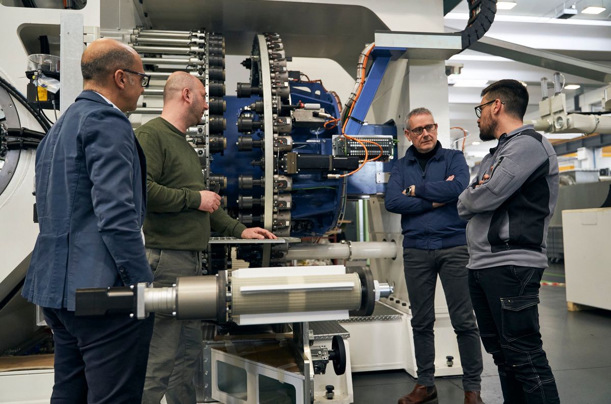 Employees from KEBA and SPL are standing together in front of a large industrial production machine in a manufacturing hall. The discussion at the machine highlights collaboration on automation, control, and industrial machinery solutions. 