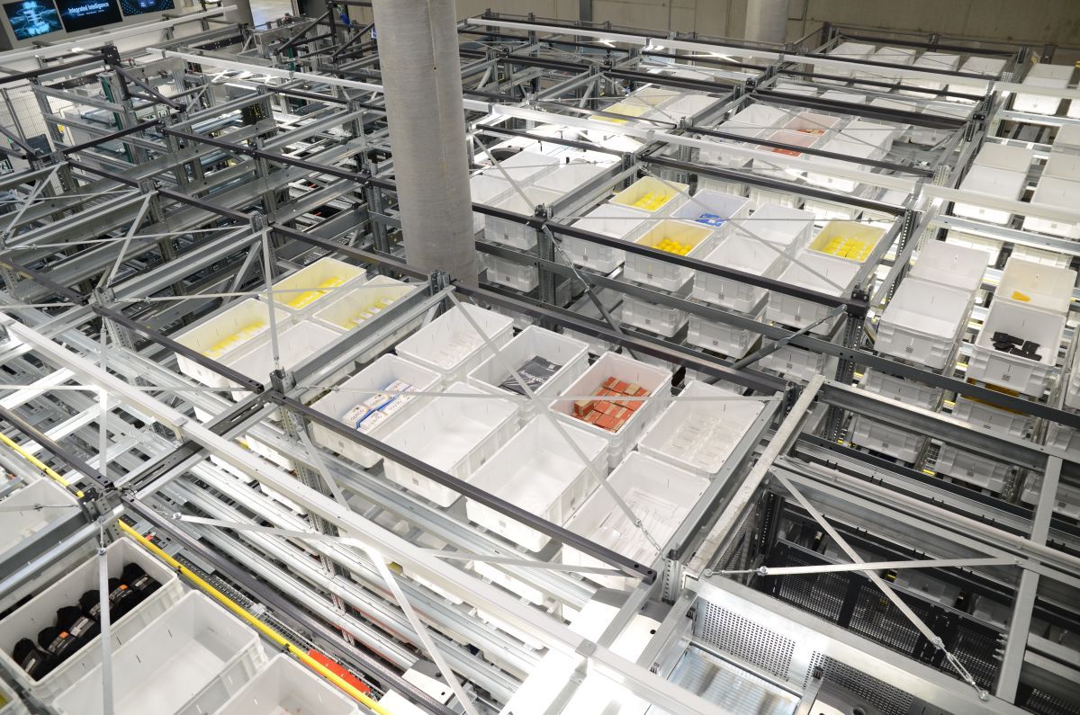 Warehouse system with stacked bins and robotic tracks for efficient storage and retrieval.