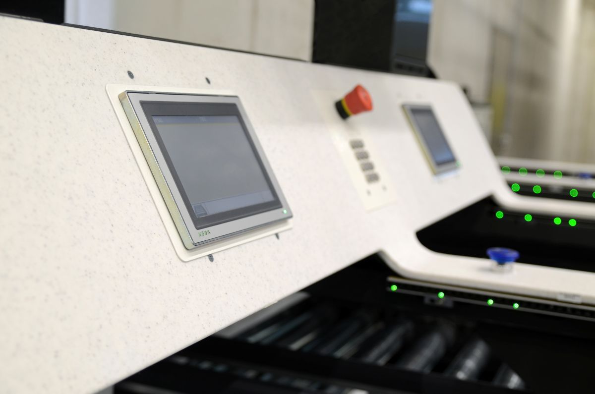 Close-up of a KEBA control panel with two touchscreens, a red emergency stop button, and green indicator lights on a machine.