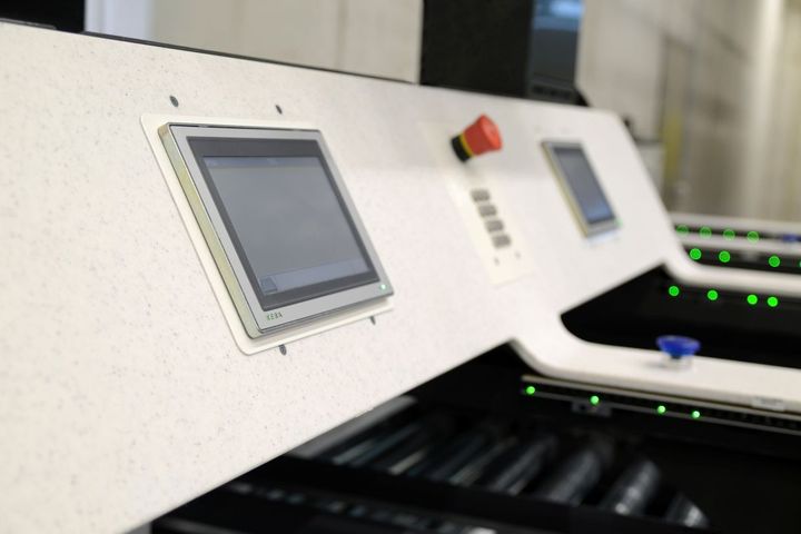 Close-up of a KEBA control panel with two touchscreens, a red emergency stop button, and green indicator lights on a machine.
