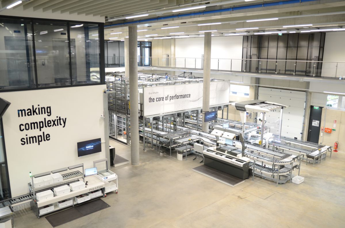 Industrial facility with conveyor systems, workstations, and banners reading "making complexity simple" and "the core of performance."