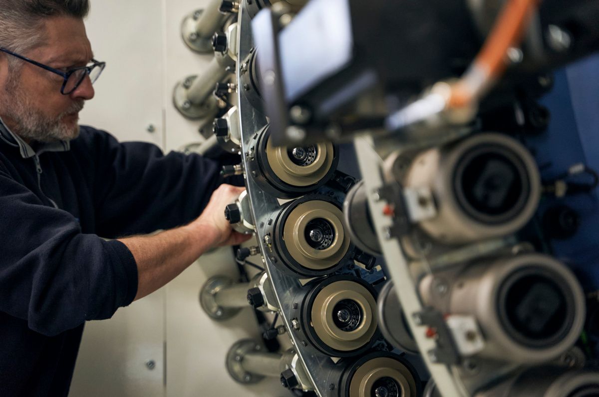 Operator working on an SPL production machine with multiple rotating spindles and material rolls in an industrial manufacturing environment. The high-performance system typically produces up to 220 cans per minute and is designed for fast and precise motion control. 
