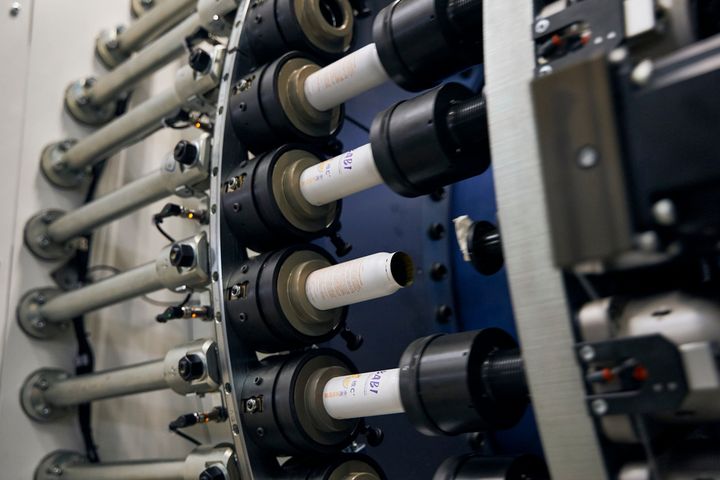 Close-up of an SPL production machine with multiple rotating spindles and wound material rolls during operation. The system handles large masses at high speed and precision for industrial automation applications.