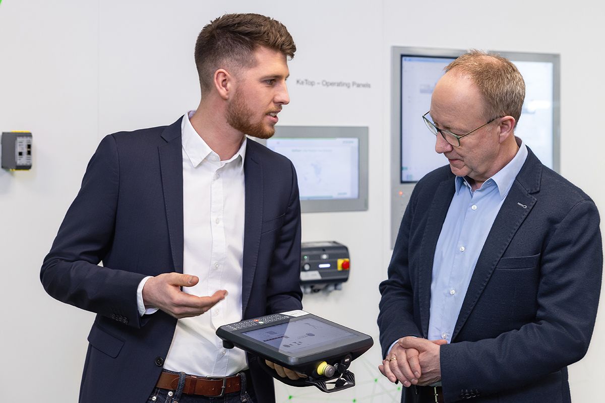 Ein KEBA-Mitarbeiter erklärt einem Kollegen die Funktionen eines Bedienpanels – technisches Know-how im Dialog.