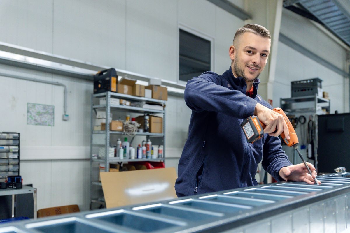 Ein KEBA-Mitarbeiter montiert mit einem Akkuschrauber ein Metallbauteil in einer Werkstattumgebung.