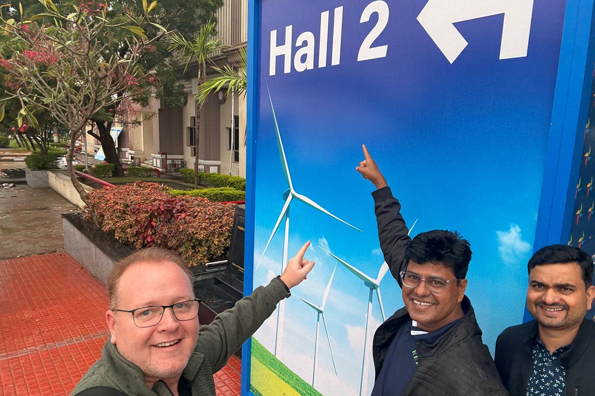 Three KEBA team members smiling and pointing at the trade fair wall "Hall 2"