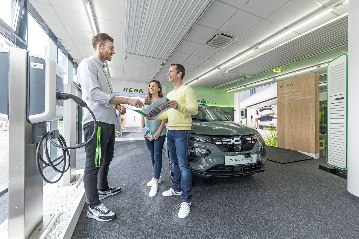 Employee talks to two customers in front of a displayed electric car.