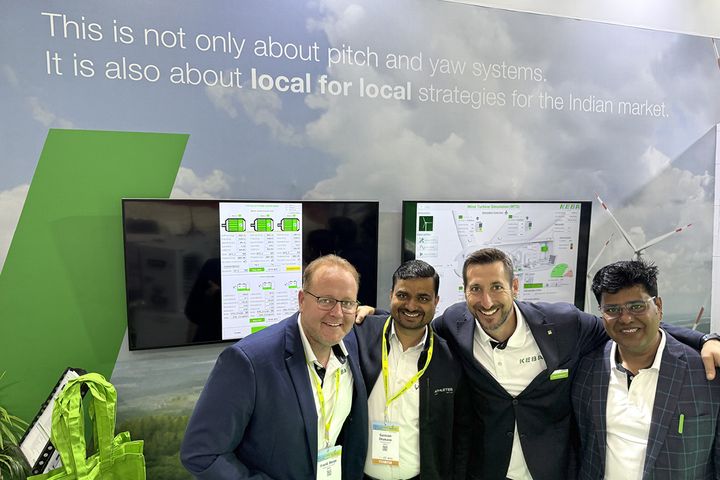 Group photo of KEBA team members standing together at a trade fair booth. The background shows the KEBA exhibition stand with white and green branding.