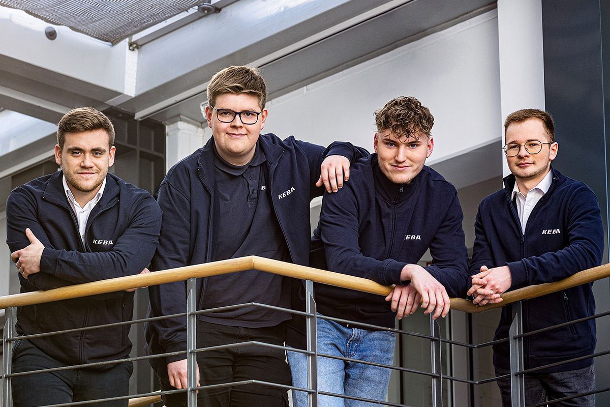 Vier KEBA-Auszubildende in Firmenkleidung posieren selbstbewusst auf einem Galeriegang – ein starkes Zeichen für Teamzusammenhalt, Nachwuchsförderung und berufliche Perspektiven in einem innovativen Unternehmen.