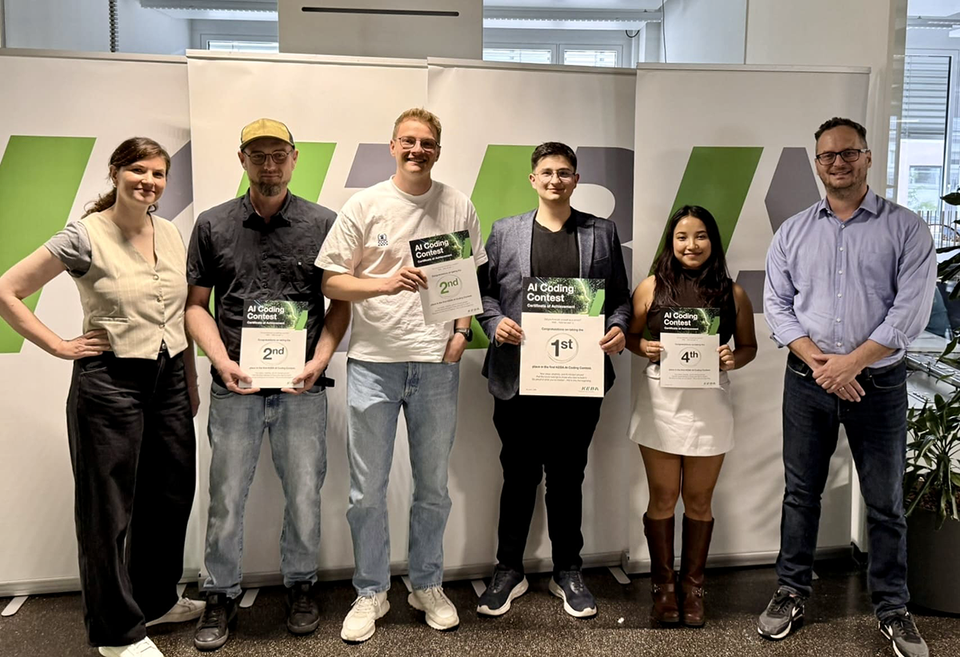 Six people stand in front of KEBA display banners indoors. Four people are holding AI Coding Contest certificates showing 1st, 2nd, 2nd, and 4th place.