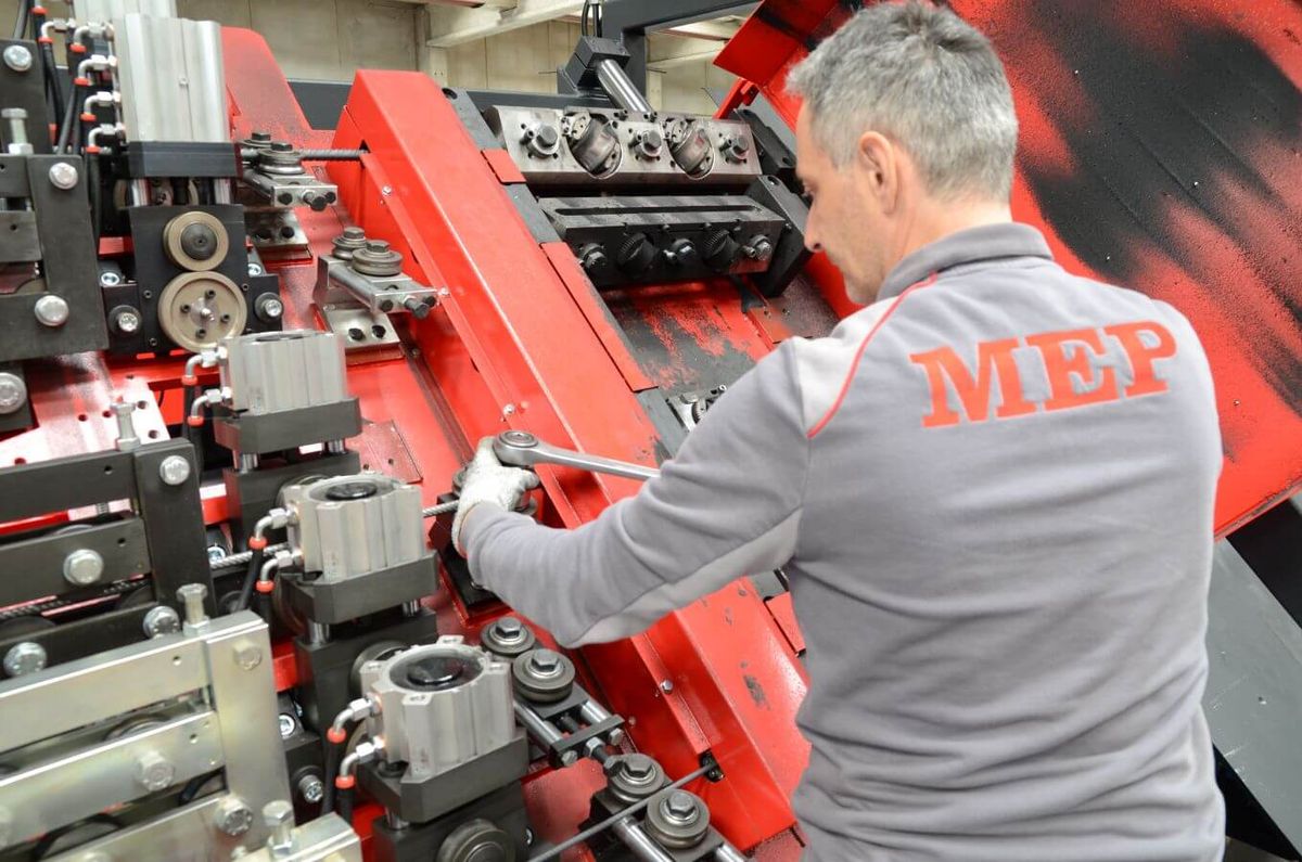 Ein Servicemitarbeiter führt Wartungsarbeiten an der Mechanik einer Maschine durch. Er justiert Komponenten mit einem Werkzeug.