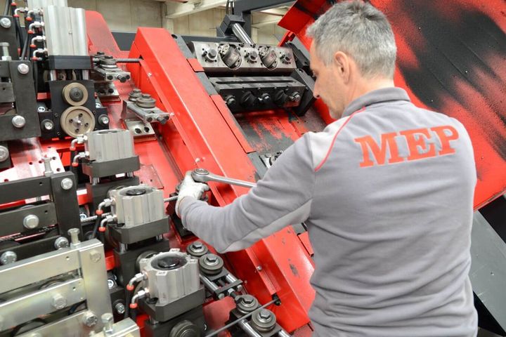 Ein Servicemitarbeiter führt Wartungsarbeiten an der Mechanik einer Maschine durch. Er justiert Komponenten mit einem Werkzeug.