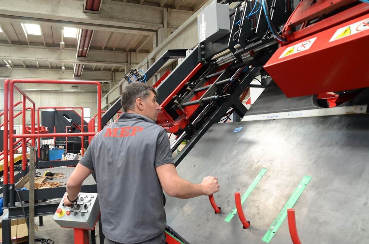 Ein Mitarbeiter bedient eine großformatige Maschine im MEP-Werk in Italien und überwacht den automatisierten Bearbeitungsprozess. Die industrielle Anlage verfügt über eine Bedienkonsole und komplexe Mechanik für präzise Materialhandhabung.