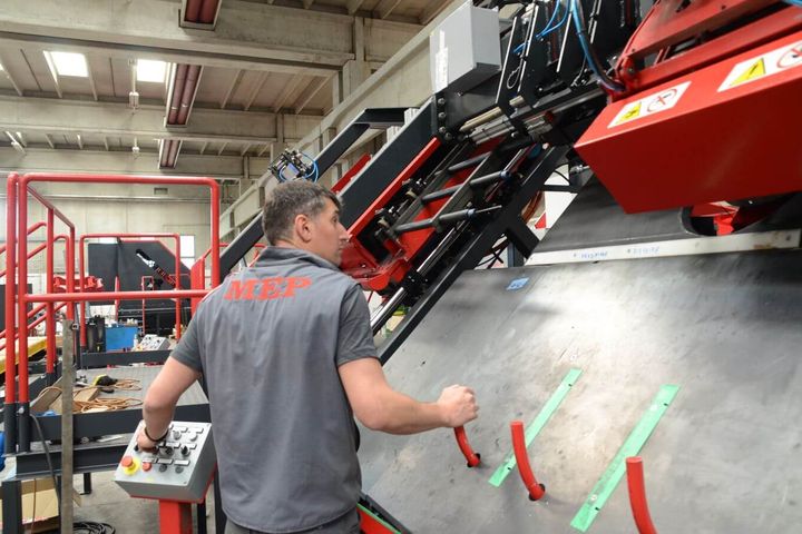 Ein Mitarbeiter bedient eine großformatige Maschine im MEP-Werk in Italien und überwacht den automatisierten Bearbeitungsprozess. Die industrielle Anlage verfügt über eine Bedienkonsole und komplexe Mechanik für präzise Materialhandhabung.