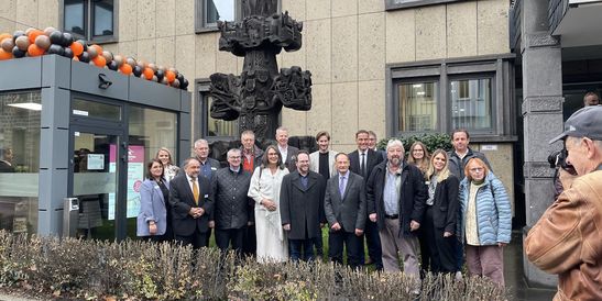 Gruppe von Personen posiert für ein Foto vor einem Gebäude mit dekorativer Skulptur und Luftballons.