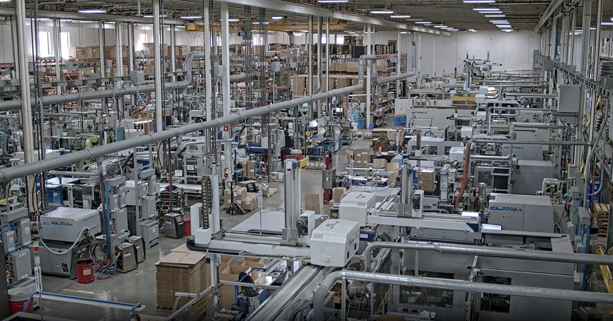 Factory Floor: Wide view of a modern factory floor filled with rows of automated injection molding machines, piping, and stacked materials.